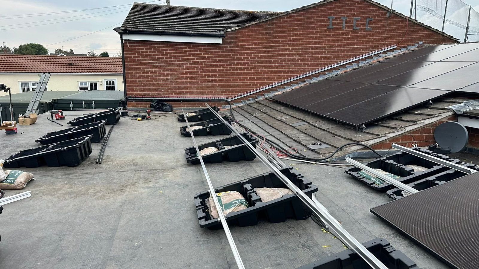 Flat roof showing three stages of a Fast Tub installation side by side: empty tubs, ballasted tubs with rails, and completed panels