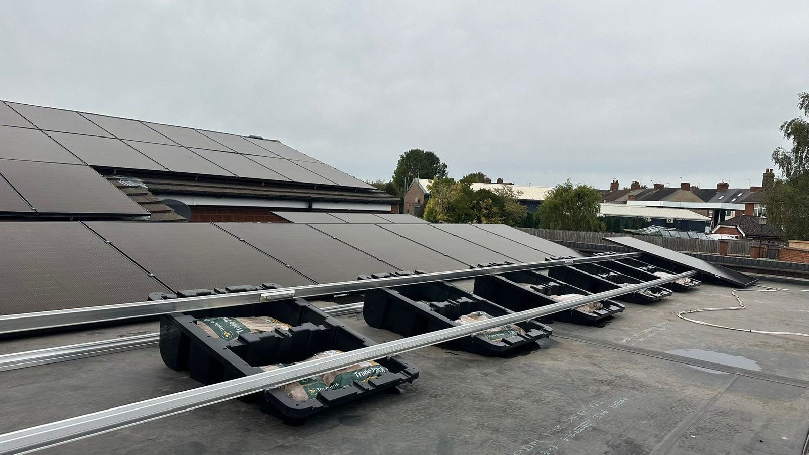 Long continuous rails linking rows of ballasted Fast Tub units into a single array on a large commercial flat roof