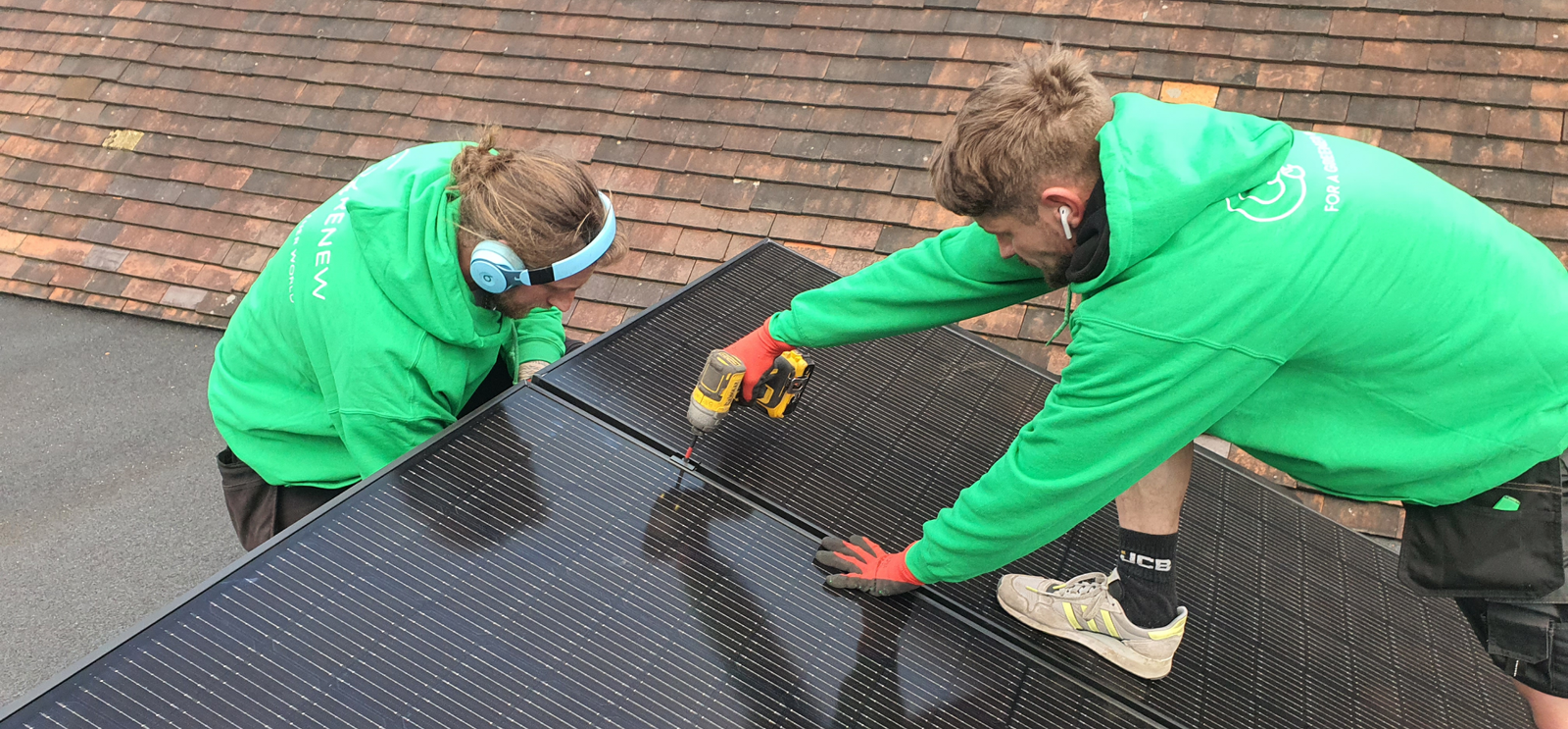 Two installers fixing portrait-orientation solar panels to the rails with an impact driver